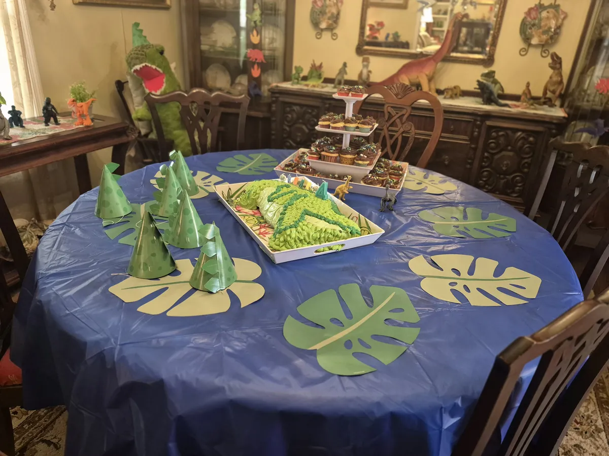 Dinosaur birthday party table decorated with green leaves and dinosaur party hats